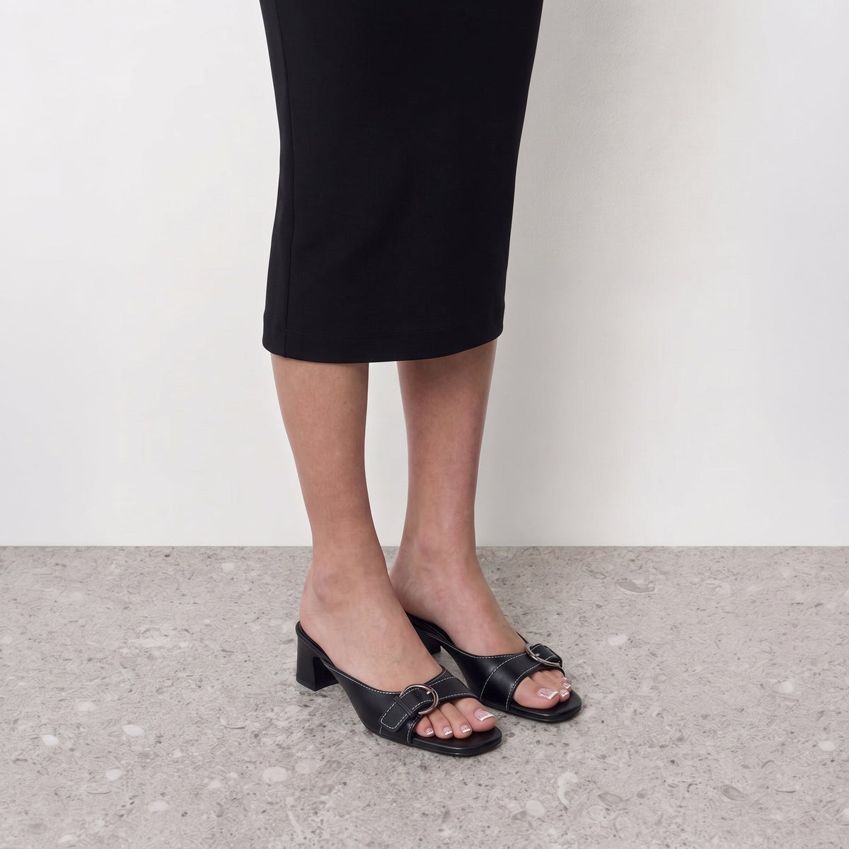 Belvra Buckle Mule Heels by Lil Cacti — on-model styled with a black midi skirt, front view of black mule heels