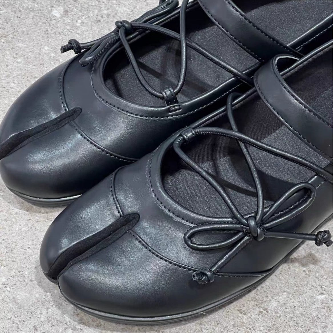 Pair of Lil Cacti black leather tabi ballet flats photographed on pale grey