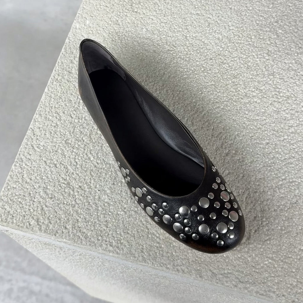 Close up of one black studded ballet flat with silver-tone studs on textured stone