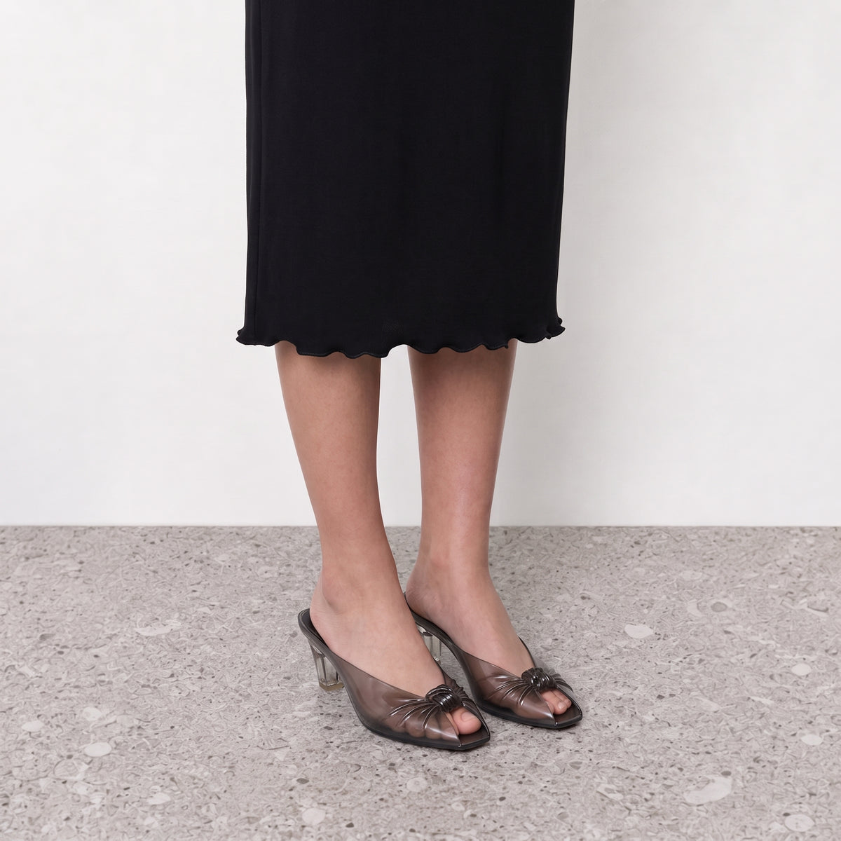 Model wearing translucent jelly mules with a clear sculpted heel