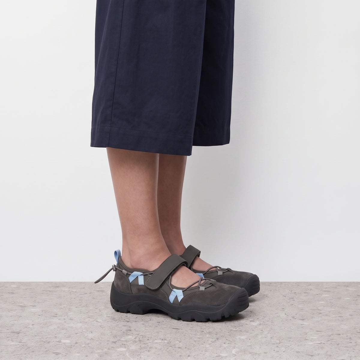 Side profile of a grey Aria mary jane sneaker worn with navy wide trousers