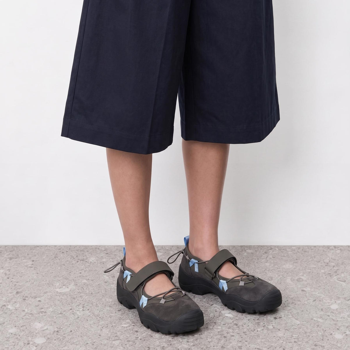 Model wearing grey mary jane sneakers with a wide hook-and-loop strap