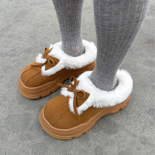 Brown slippers with white fur lining worn by a person on a concrete surface