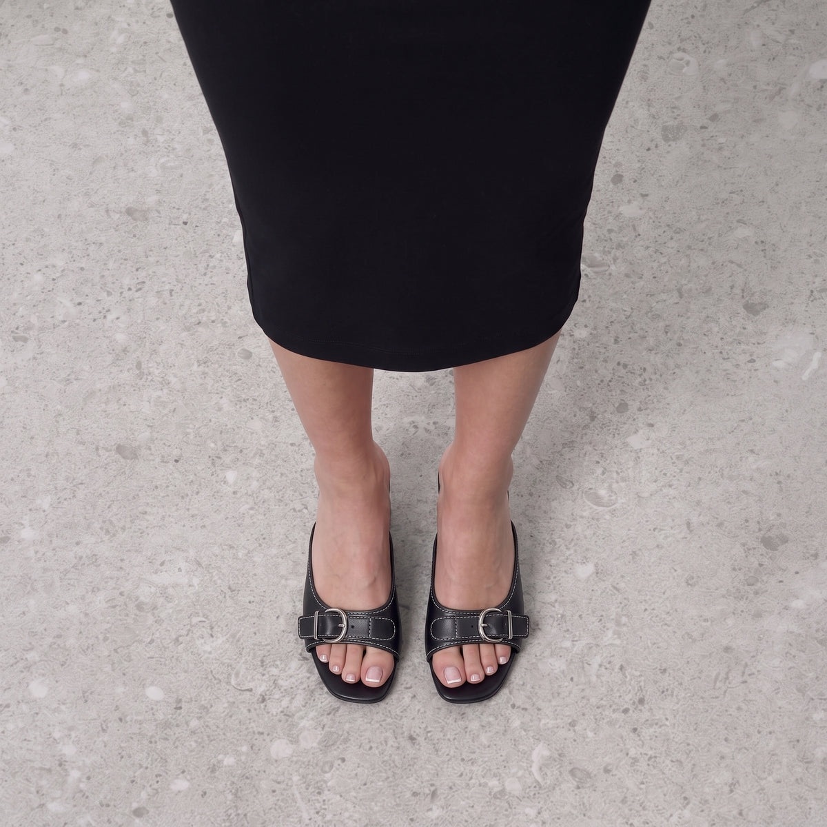 Front view on the foot of black buckle mules on a low block heel