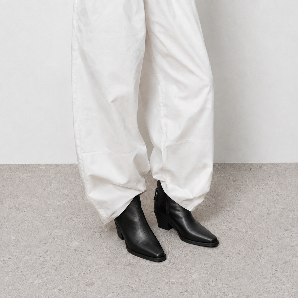 Black pointed toe western boots with a V-cut topline on a wood floor