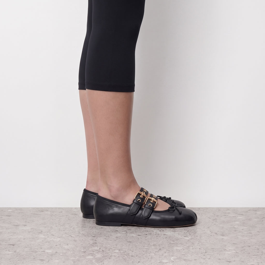 Side profile of a black buckle strap ballet flat worn with cropped black leggings