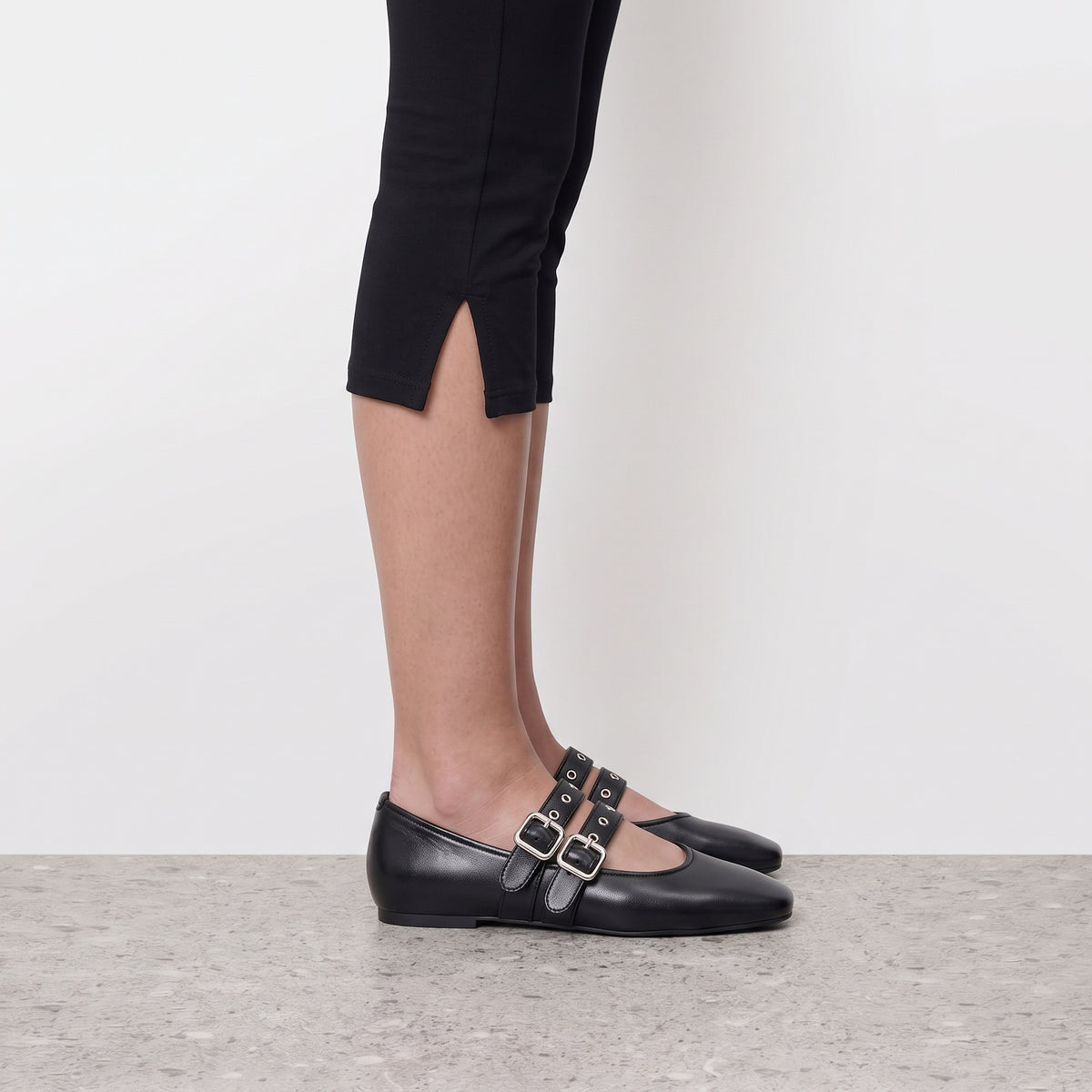 Side profile of a black double buckle mary jane flat worn with cropped black leggings