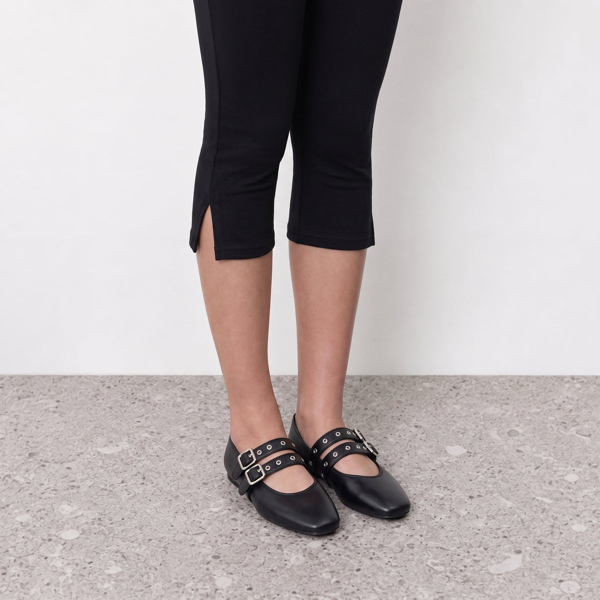 Model wearing black double buckle mary jane ballet flats on a stone floor
