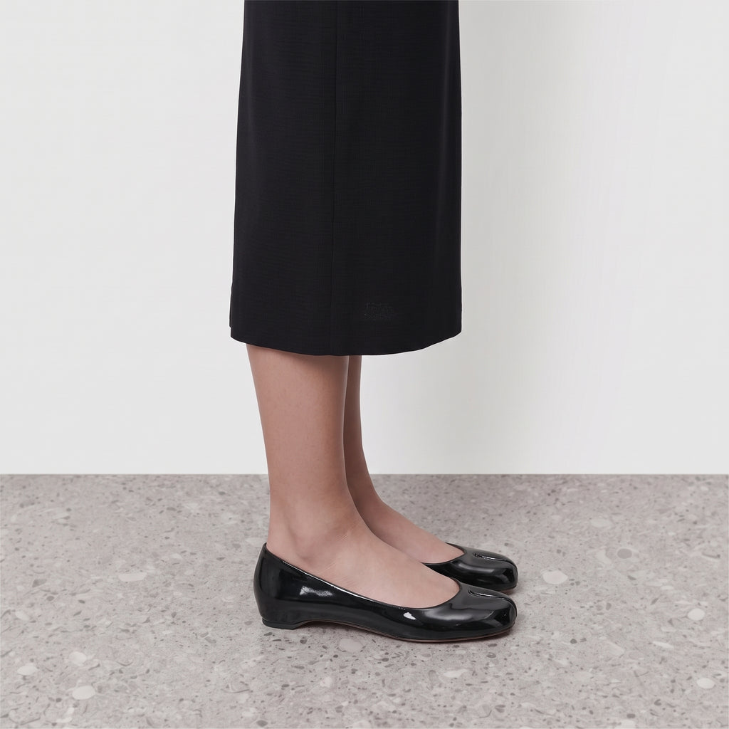 Side profile of a black patent tabi flat worn with a black skirt