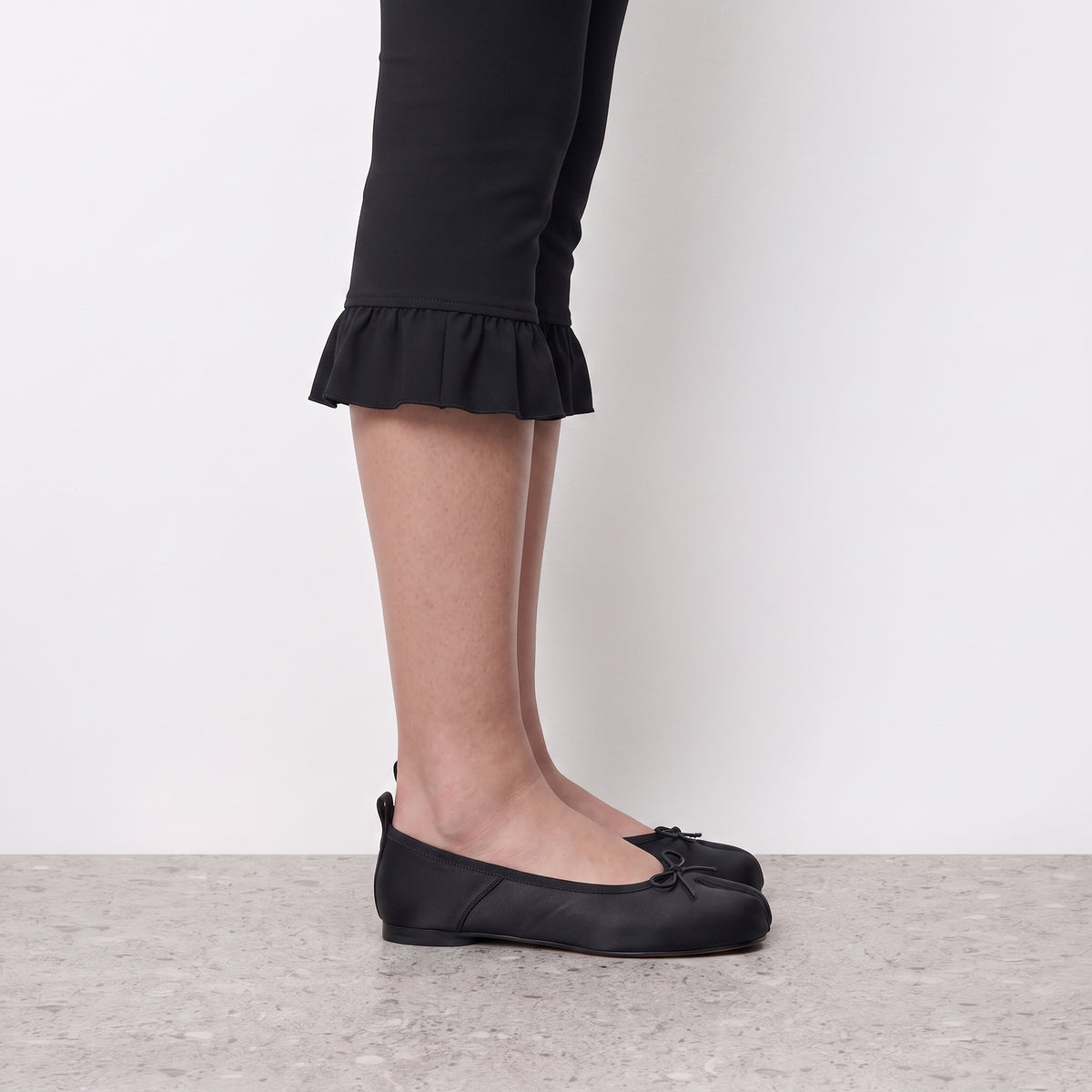 Side profile of a black satin tabi flat worn with ruffled-hem cropped leggings
