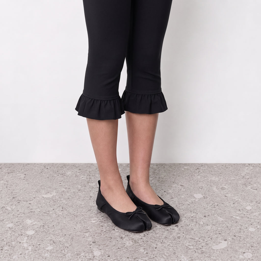 Model wearing black satin split toe ballet flats on a stone floor