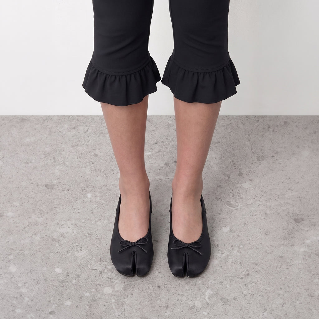 Front view on the foot of black satin tabi flats with the drawstring bow