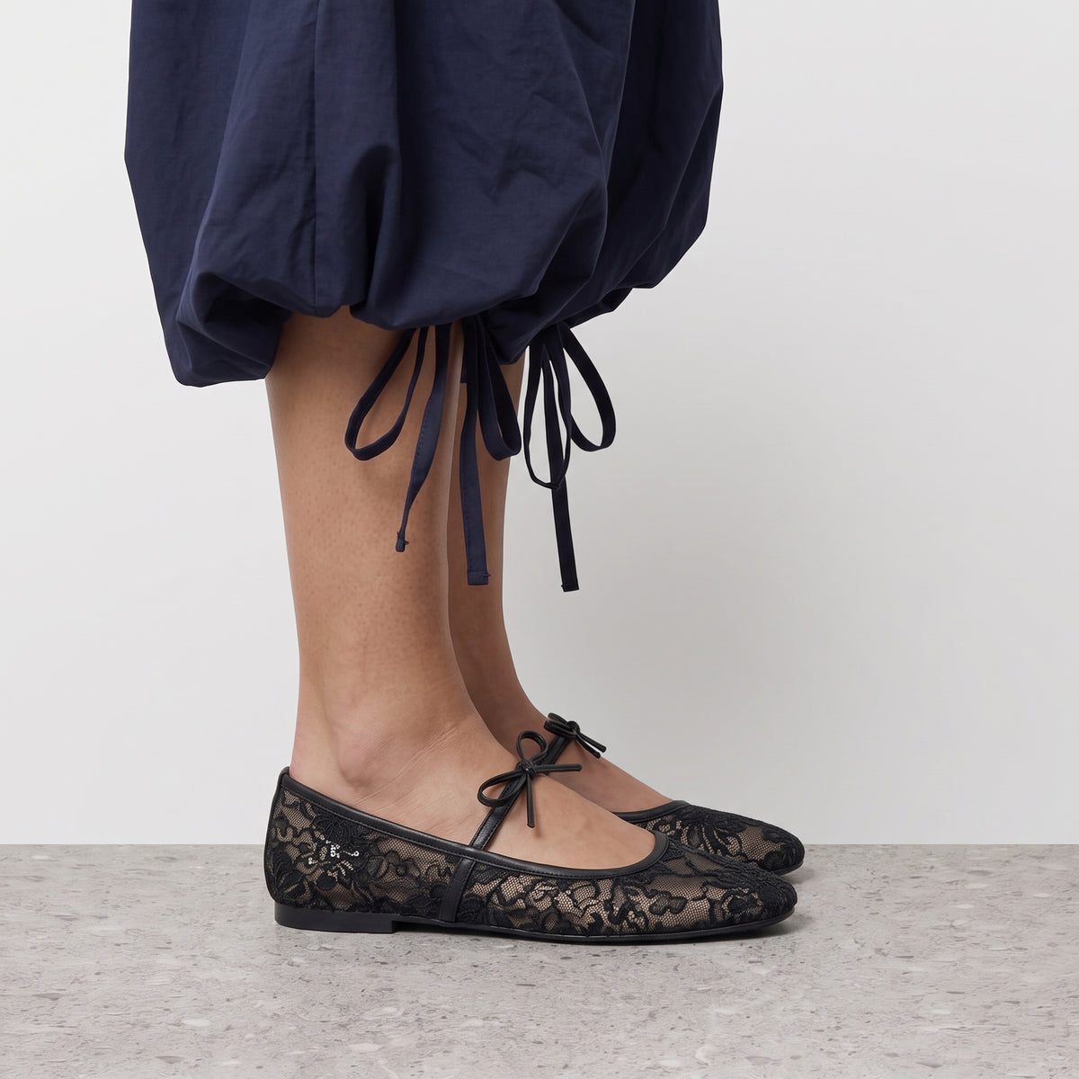 Side profile of a black sheer lace ballet flat worn with a navy bubble-hem skirt