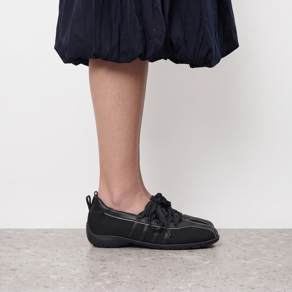 Side profile of a black Iris lace-up sneaker flat worn with a navy bubble-hem skirt