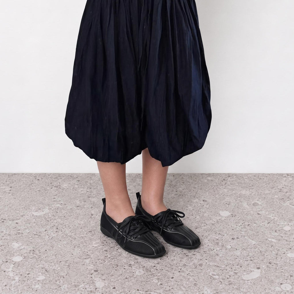 Model wearing black square toe ballet sneakers with front lacing