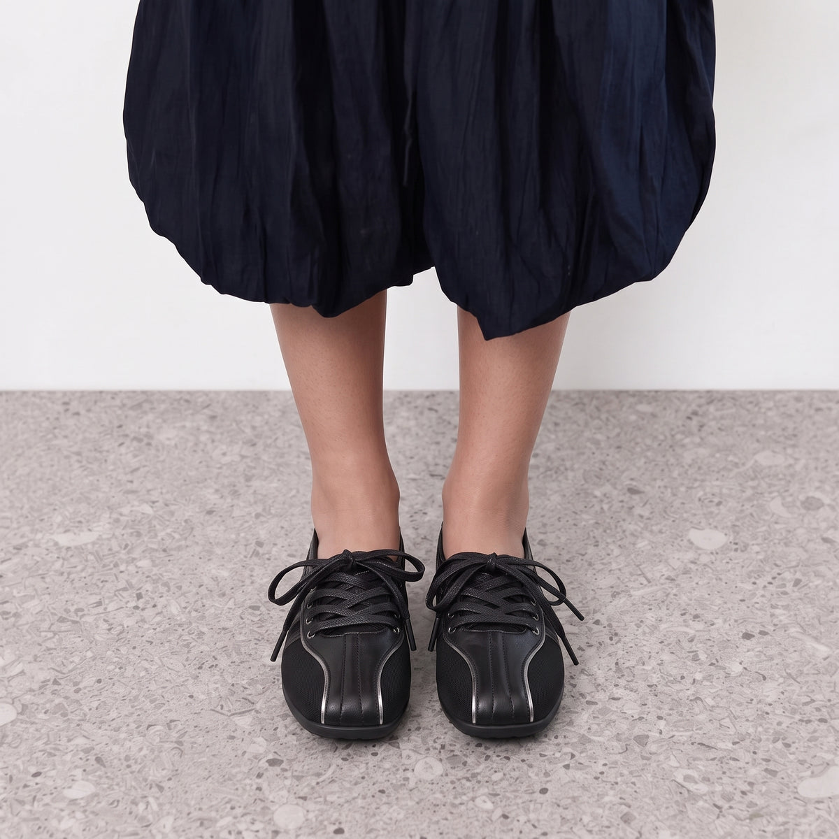 Front view on the foot of black lace-up sneaker flats with silver piping