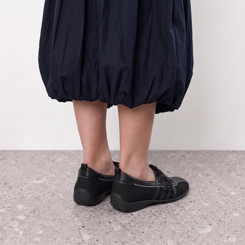 Model standing in Lil Cacti black Iris sneaker flats on a stone floor