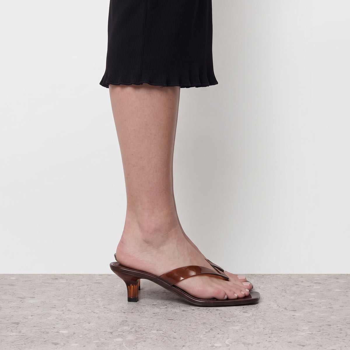 Side profile of a brown translucent thong sandal on a kitten heel worn with a black skirt