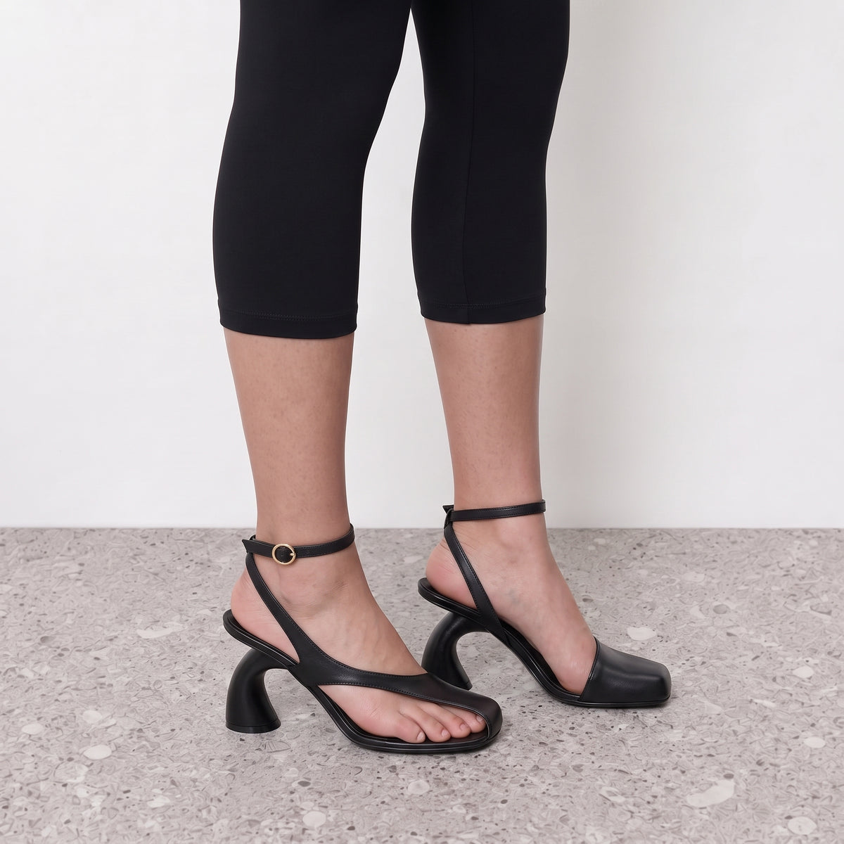 Side profile of a black strappy sandal heel with an ankle strap and sculpted heel