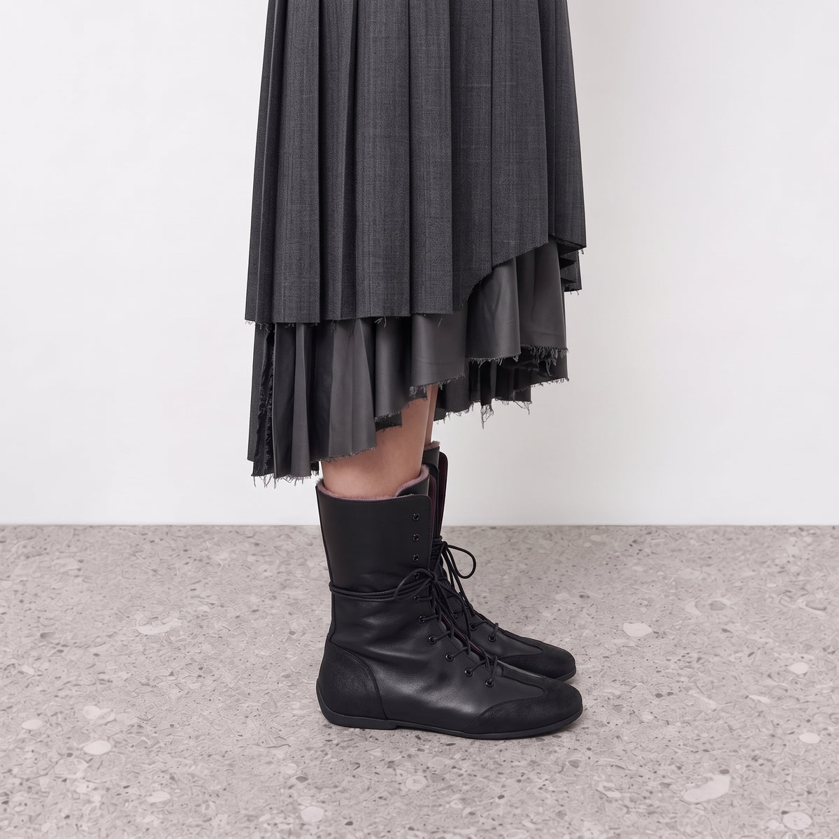 Ottilie black lace-up combat boots worn with a grey pleated skirt, side view