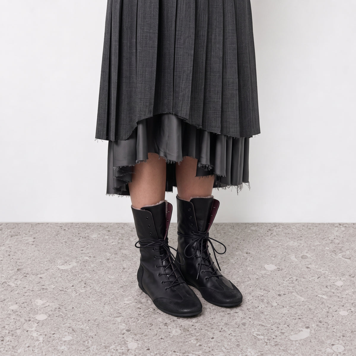 Model wearing Ottilie lace-up combat boots with a grey pleated midi skirt