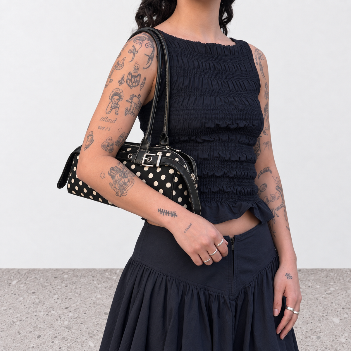 Polka dot baguette bag held at the hip with a black ruched top and navy skirt
