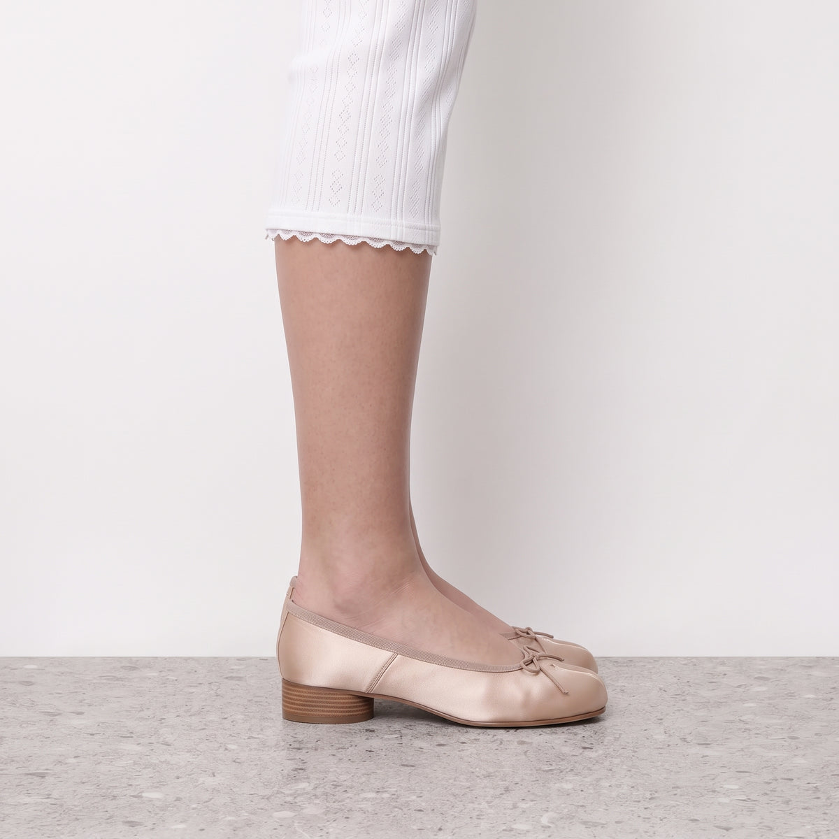 Side profile of a champagne split toe ballerina pump worn on a stone floor