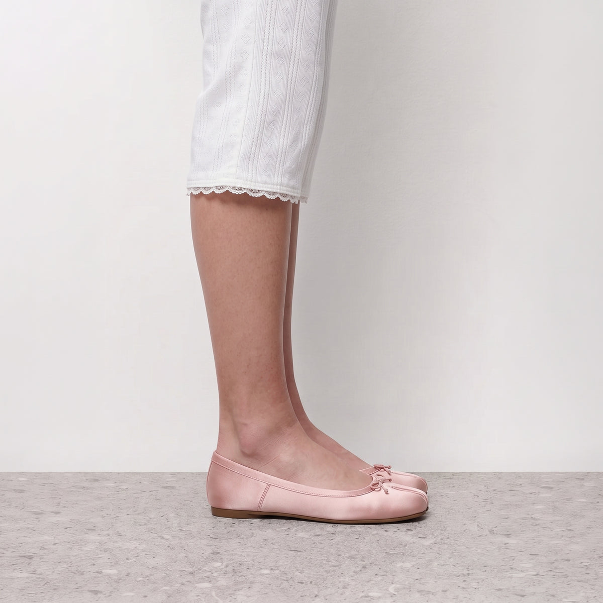 Side profile of a blush pink satin tabi flat worn with white ribbed cropped trousers