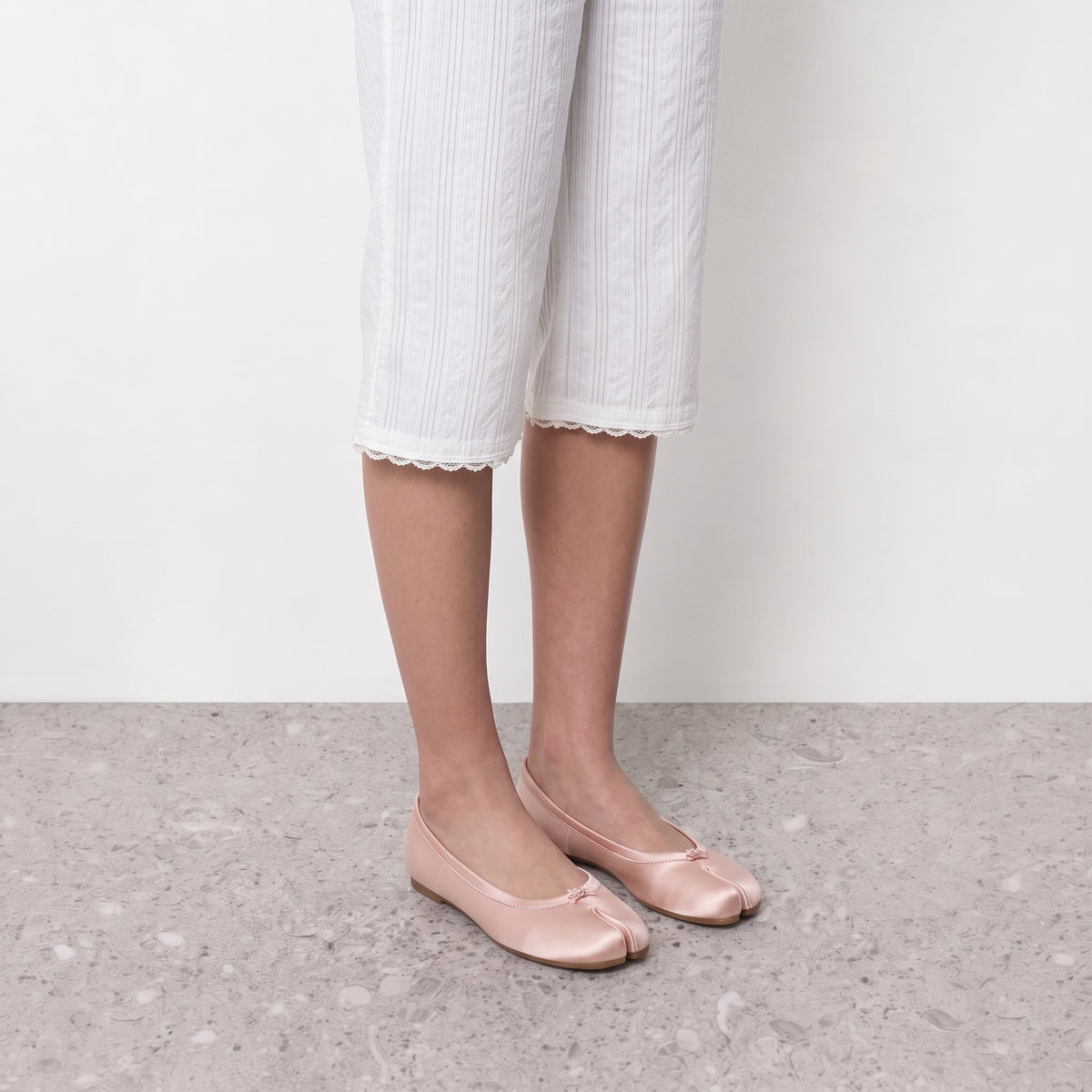 Model wearing blush satin split toe ballet flats on a stone floor