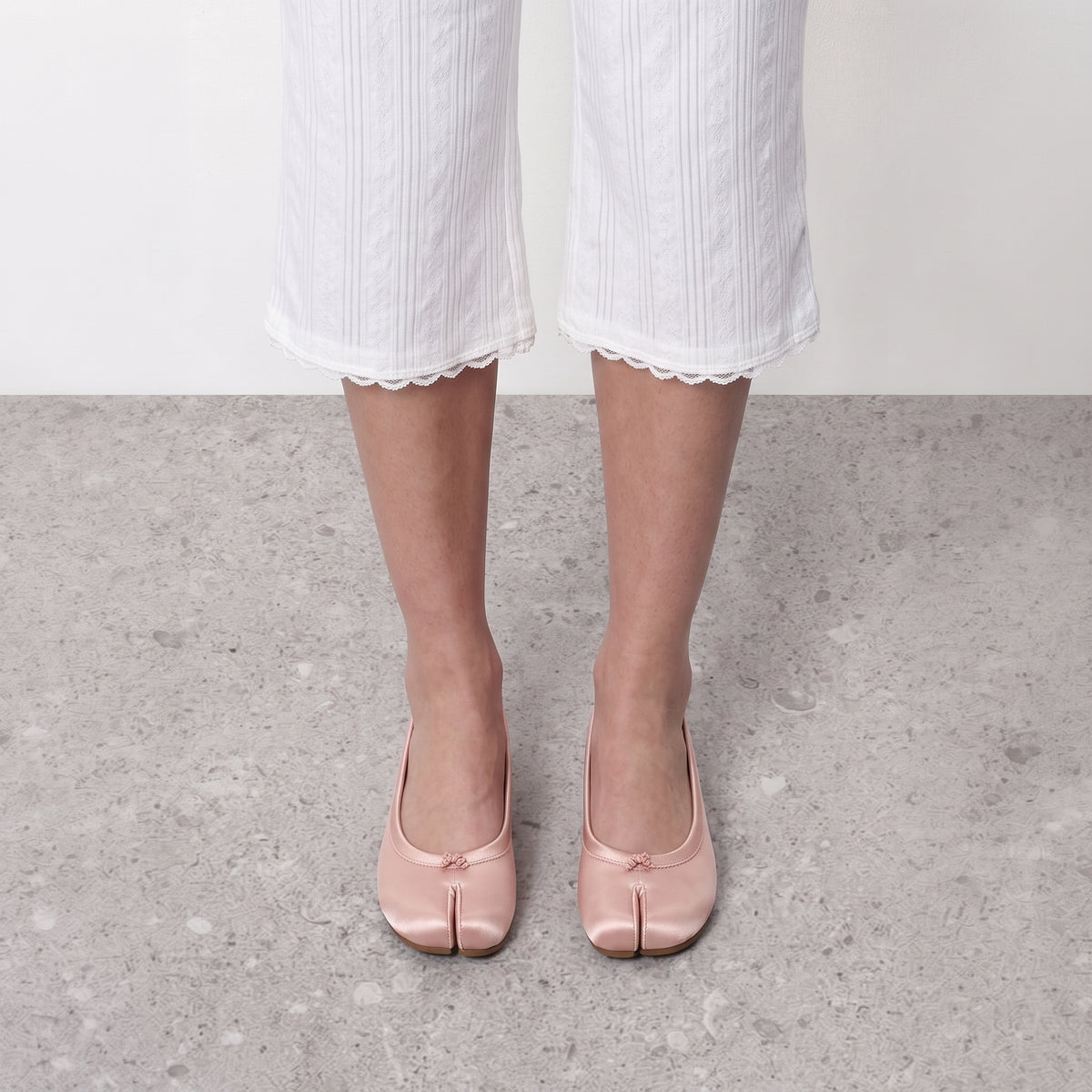 Front view on the foot of blush satin tabi flats showing the divided toe and bow