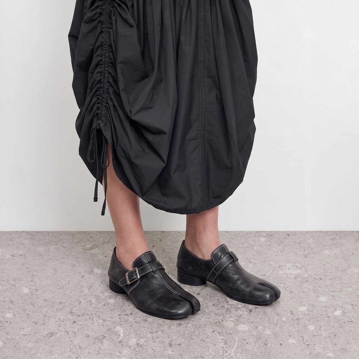 Model wearing black split toe loafers with a silver buckle