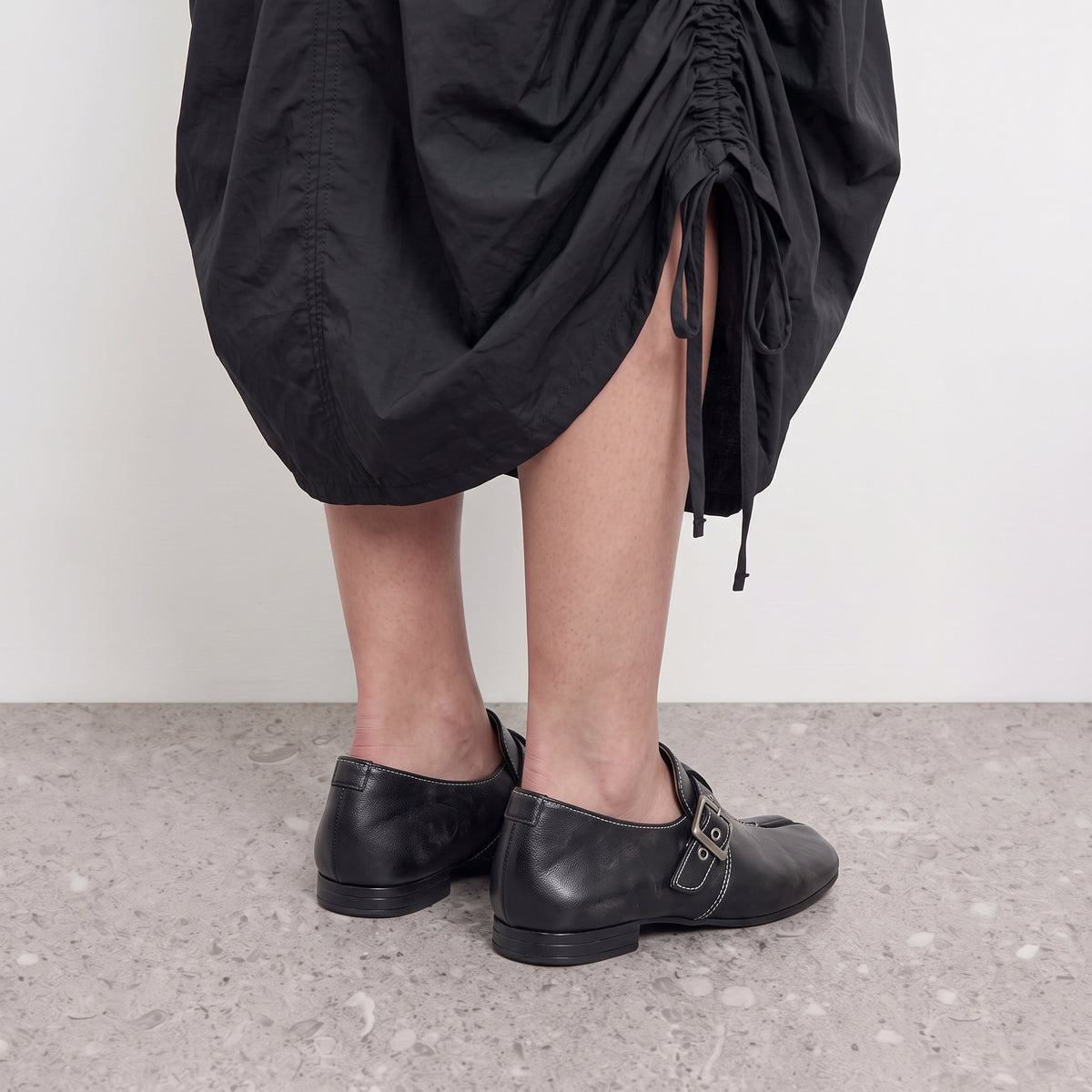 Model standing in Lil Cacti Rue black tabi loafers on a stone floor