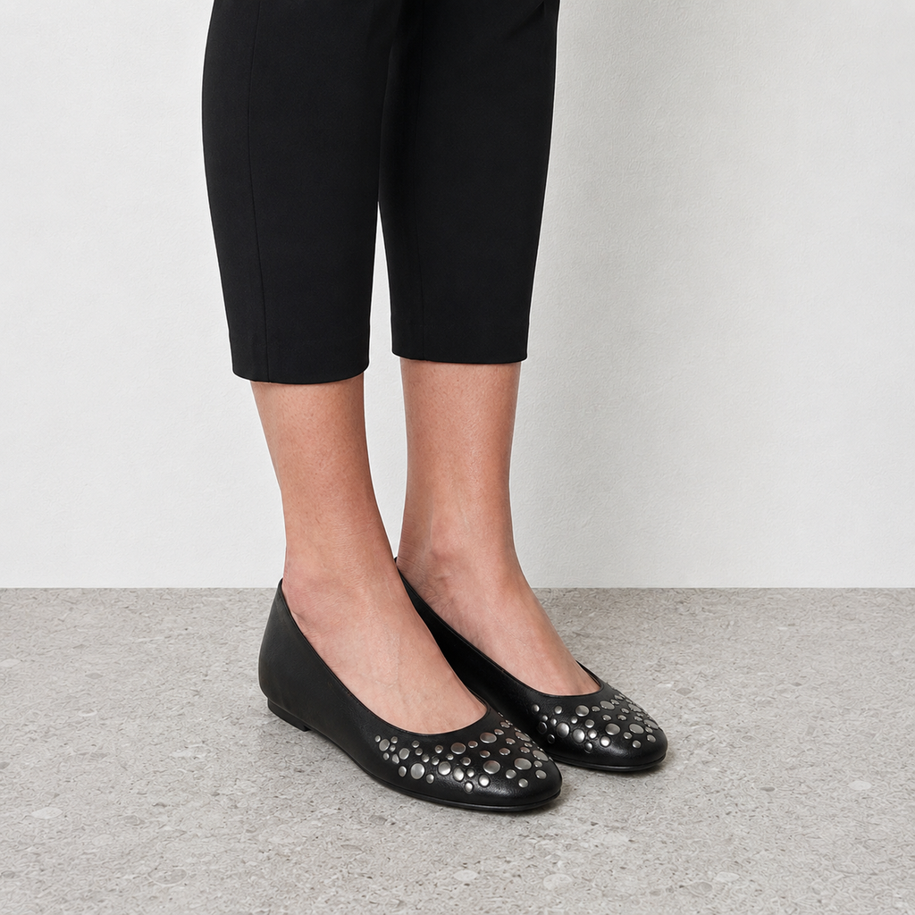 Model wearing black studded ballet flats with cropped black pants on stone floor
