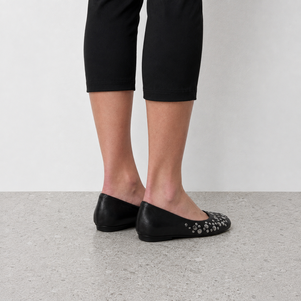 Front angle of black studded ballet flats worn with bare ankles and cropped black pants