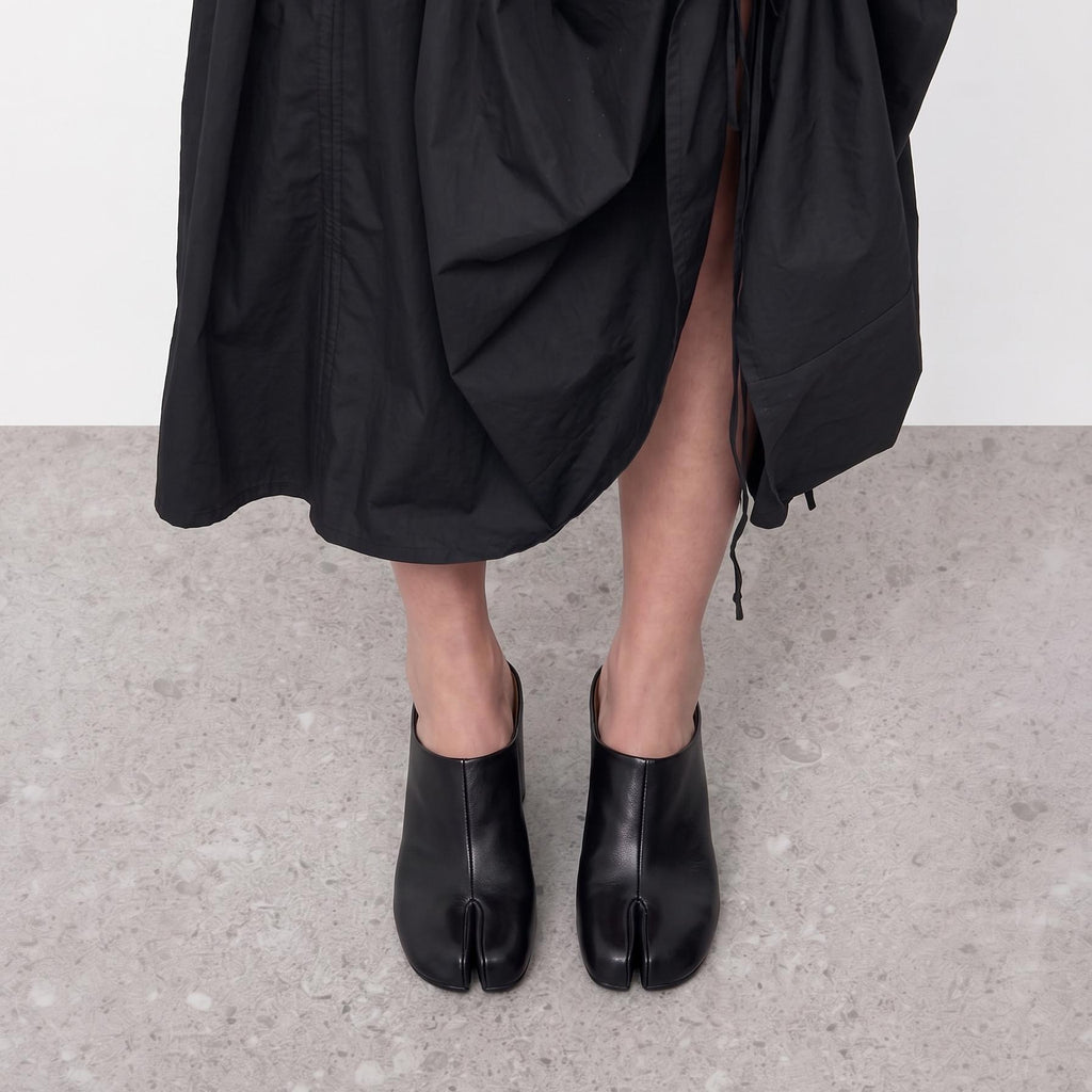 Feet in black tabi mules viewed from the front, black skirt hem visible