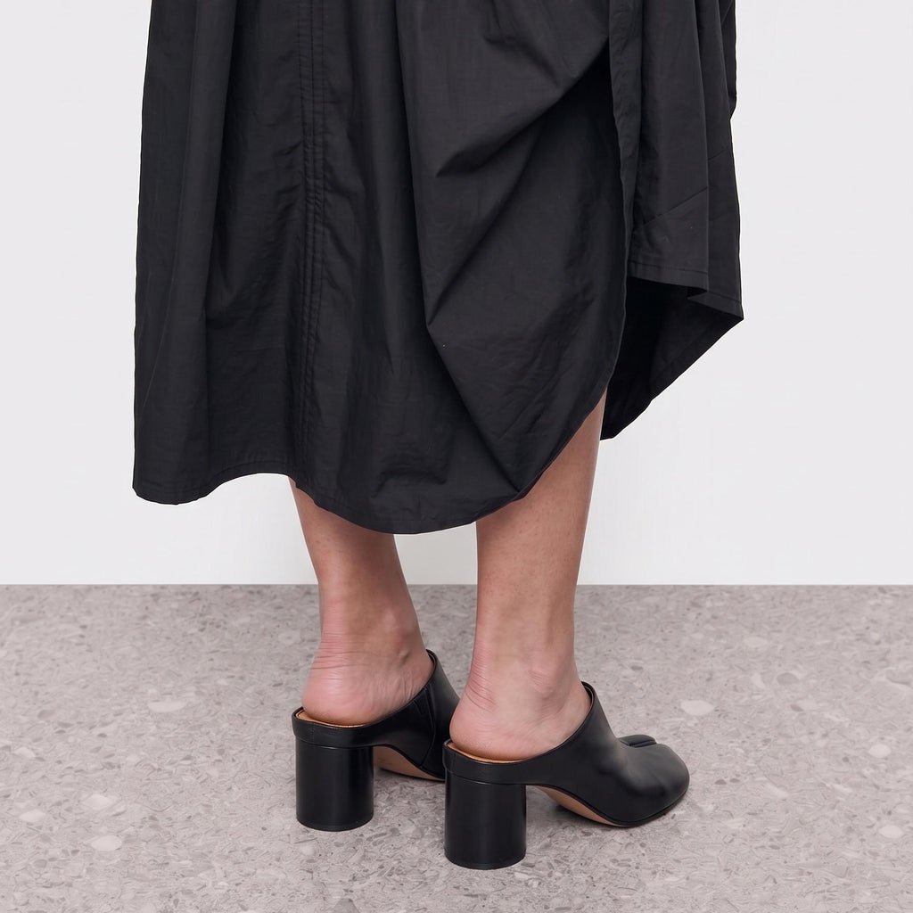 Model standing in black tabi mules, side view showing the block heel