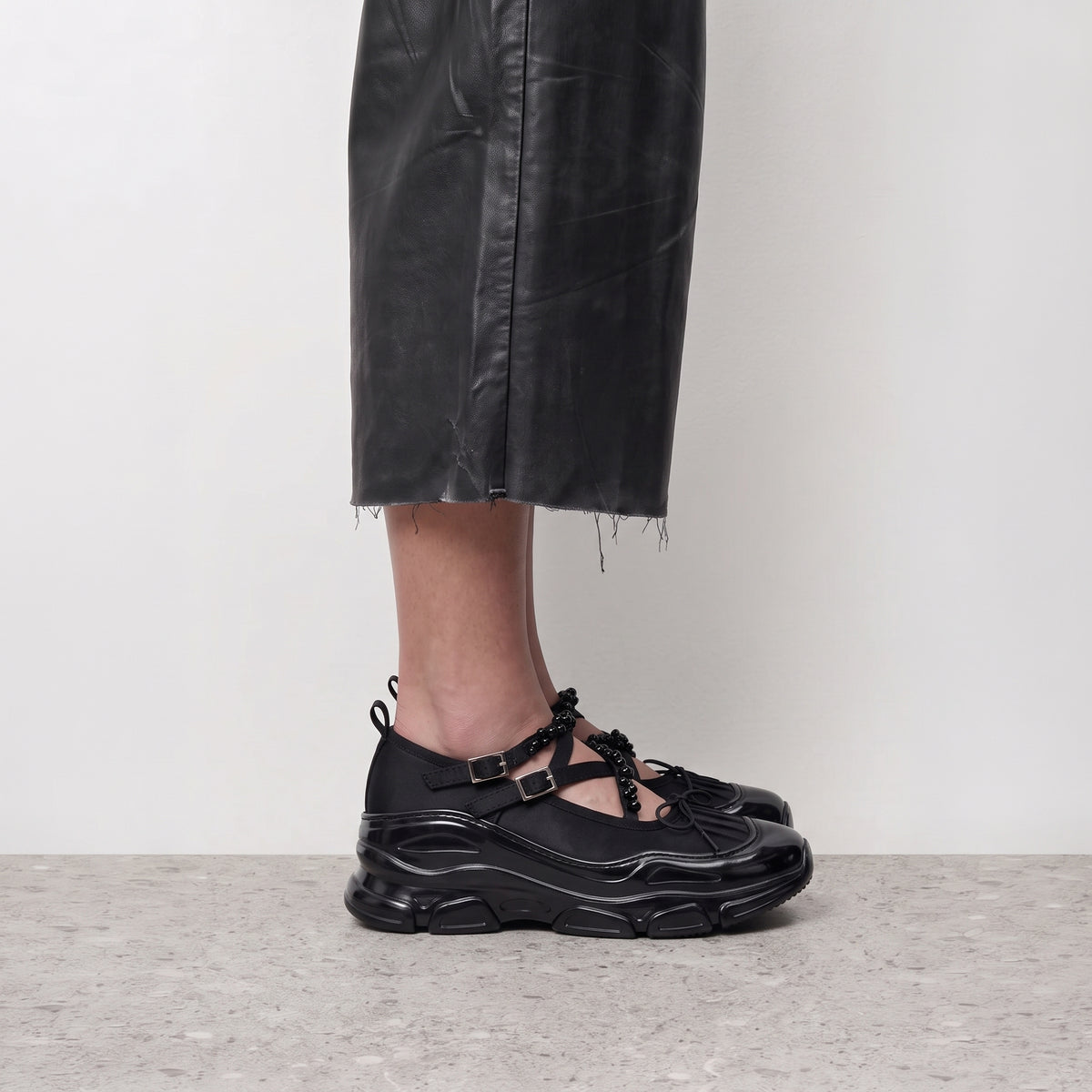Side profile of a black Velvet Barre ballet sneaker worn with a leather-look midi skirt