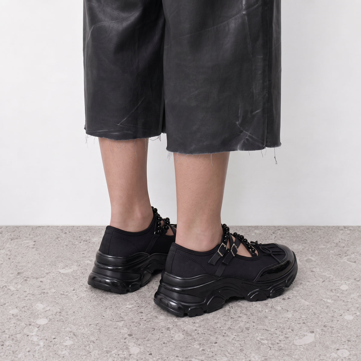 Model standing in black Velvet Barre ballet sneakers with a raw-hem leather-look skirt
