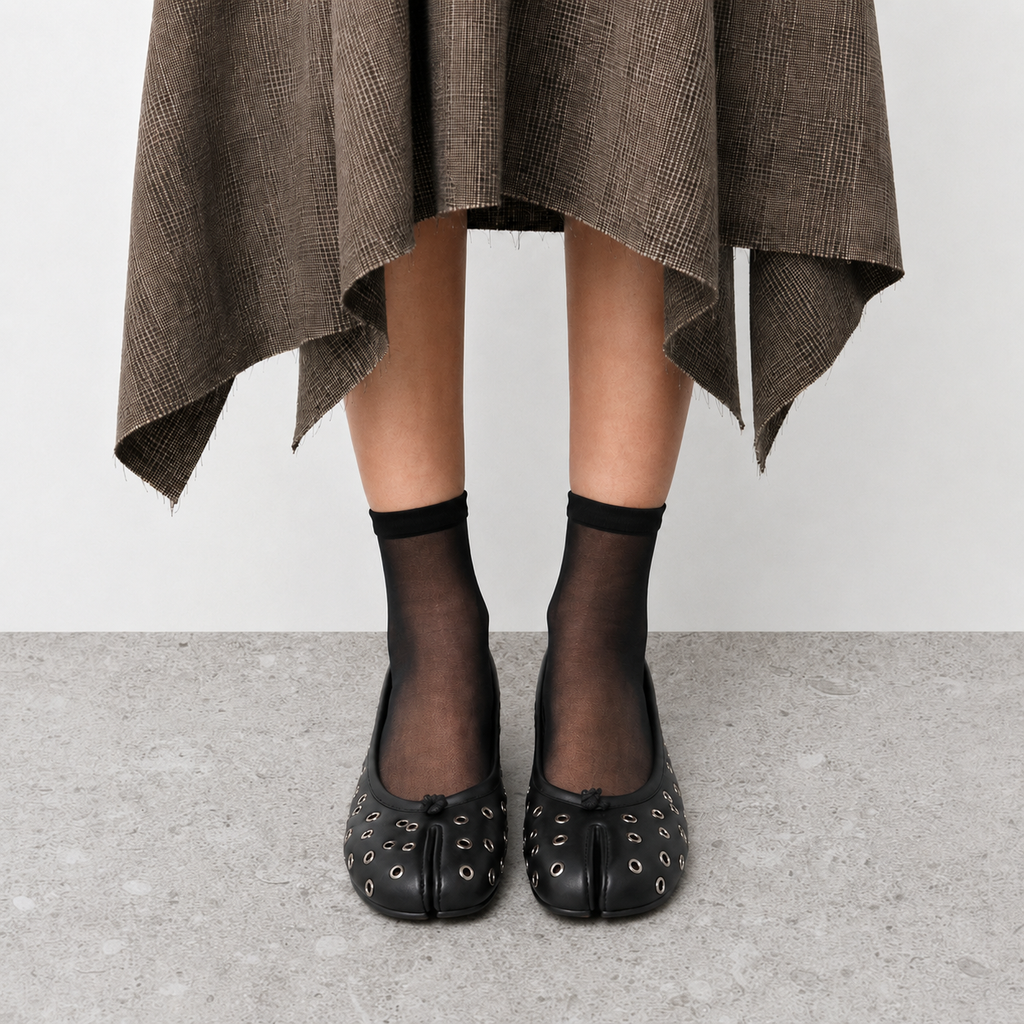 Side view on foot of black tabi flats worn with sheer socks on stone