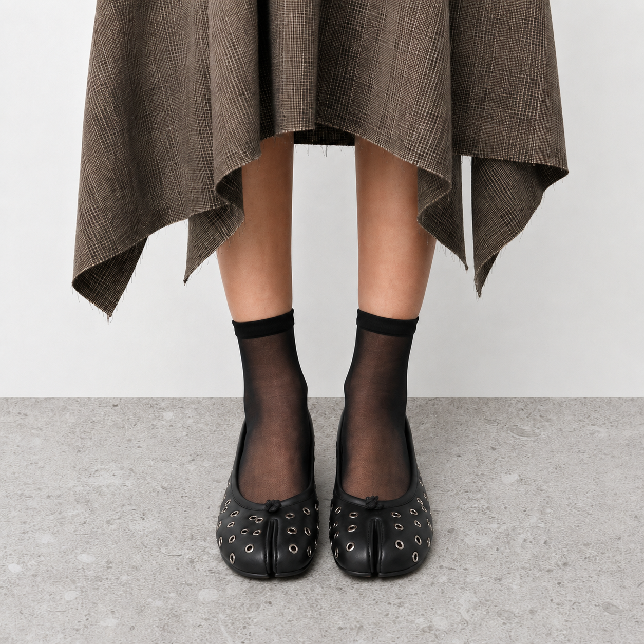 Side view on foot of black tabi flats worn with sheer socks on stone