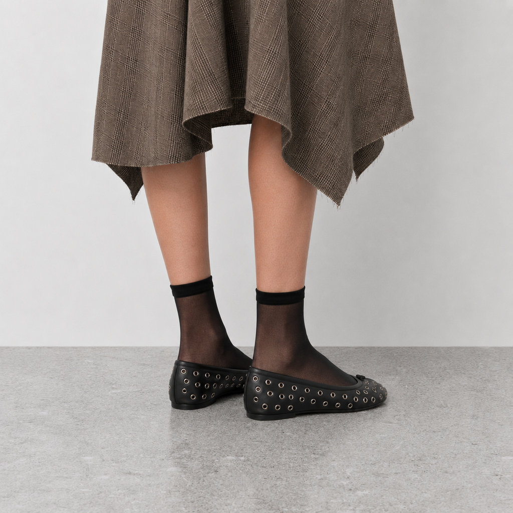 Front view of black eyelet tabi flats worn with sheer socks, split toe visible