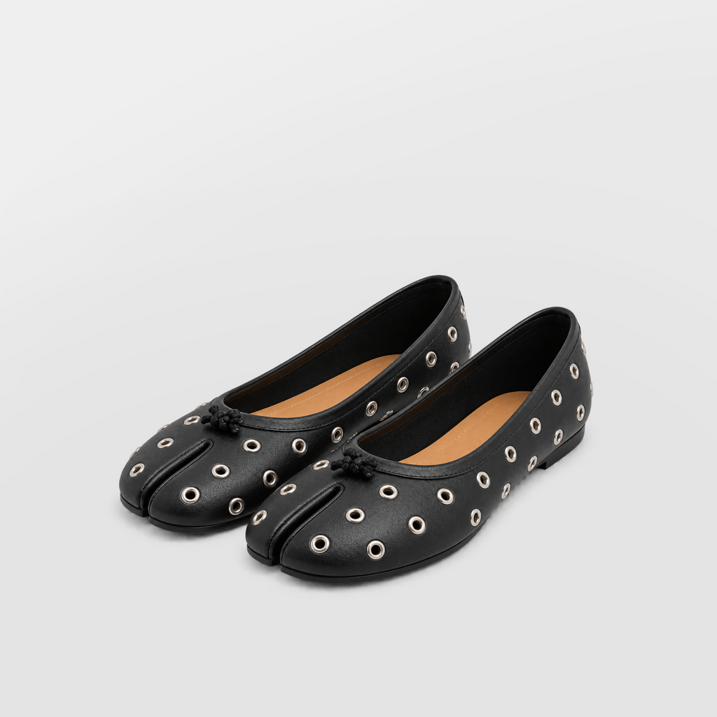 Rear side angle of black eyelet tabi flats with sheer socks under draped brown hem