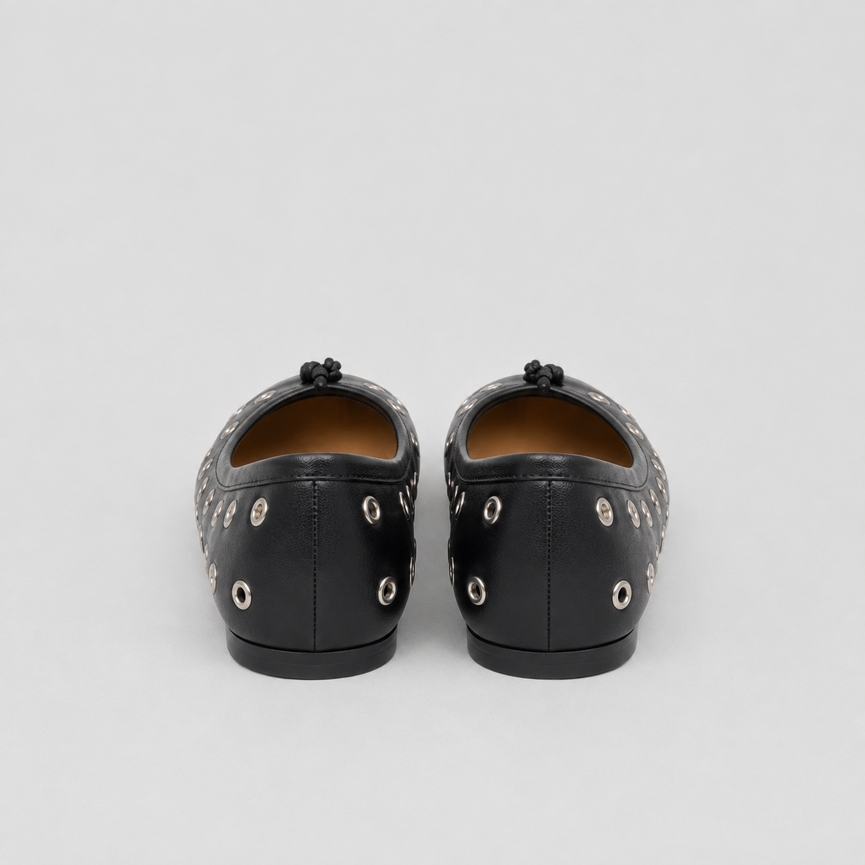Back view of black eyelet flats, silver grommets on heel sides, plain center seam