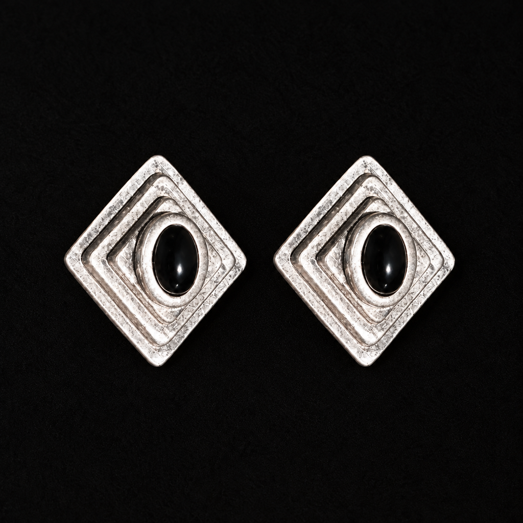 Close front view of Ziggurat Stepped Stud Earrings, dark-silver art deco stud earrings with a black oval stone on a dark background