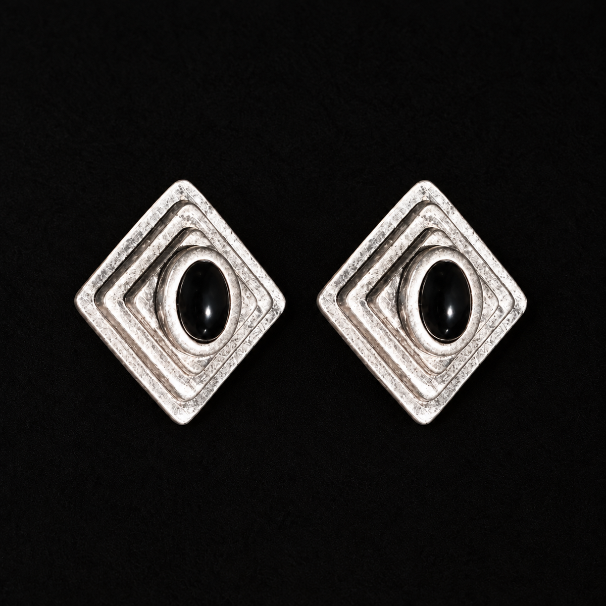 Close front view of Ziggurat Stepped Stud Earrings, dark-silver art deco stud earrings with a black oval stone on a dark background