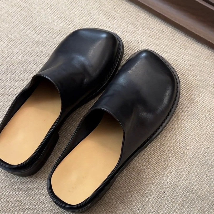 Pair of black square-toe mules on a beige rug, front view